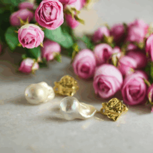 Pair of Baroque Tide Earrings with irregular baroque pearls and gold-plated brass details, displayed under soft, warm lighting. Be the Gliding Grace.