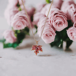 Gold-tone maple leaf pendant necklace with red crystal center on fine chain. Be the gliding grace.