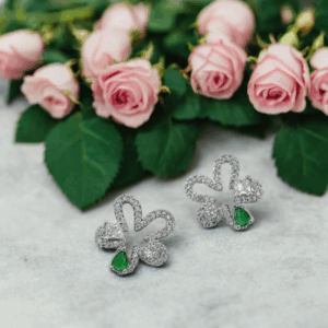 Four-leaf clover-shaped stud earrings with green and white stones on neutral background. Be the gliding grace.